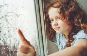 Niña feliz dibujando un corazón en la ventana