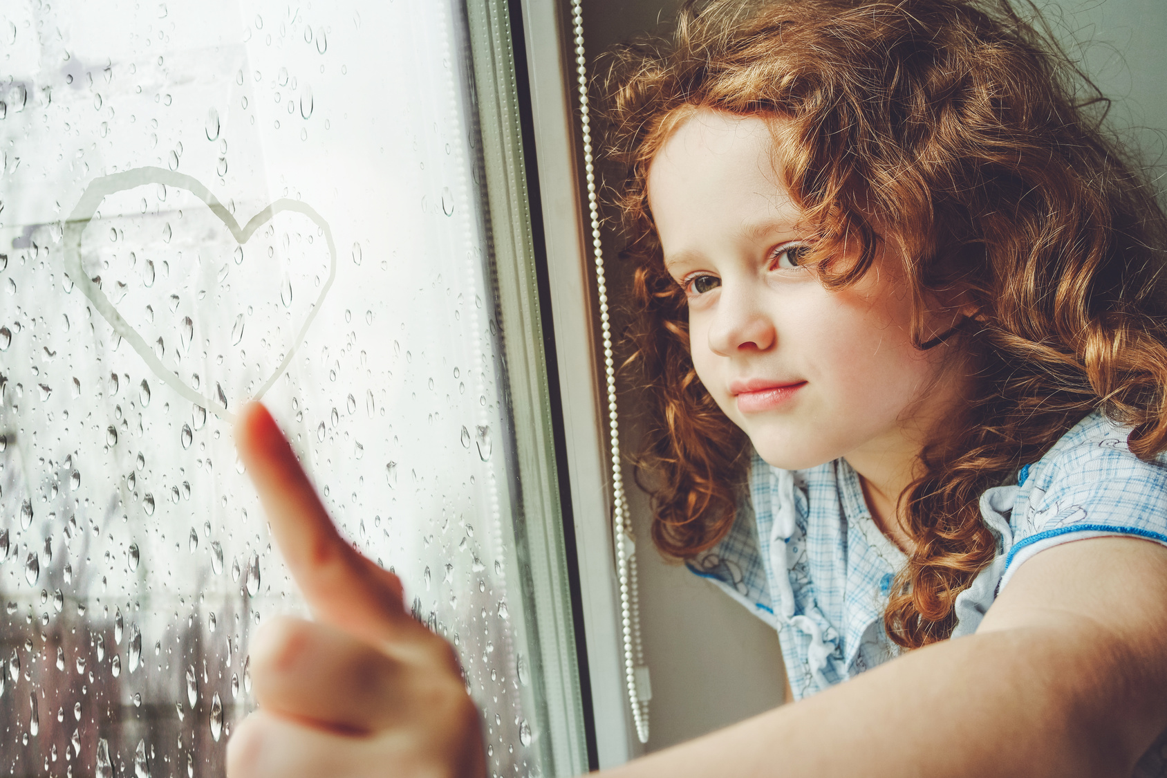 Niña feliz dibujando un corazón en la ventana