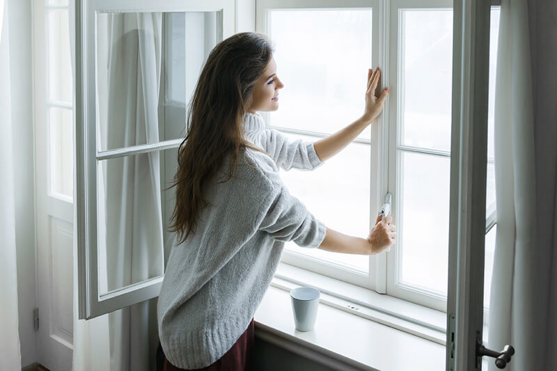 Mujer abriendo las ventanas para ventilar el hogar.